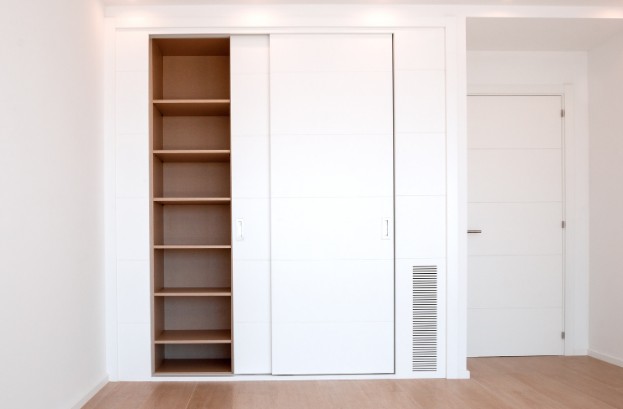 Armario empotrado a medida con puertas correderas blancas y estantería de madera en un dormitorio de Málaga