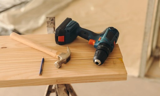 Atornillador y martillo de carpintero sobre un tablero de madera durante un montaje de muebles