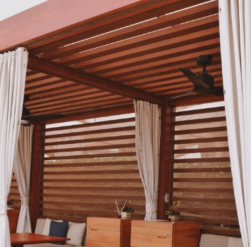 Pérgola de lamas de madera con cortinas laterales y ventilador en un porche